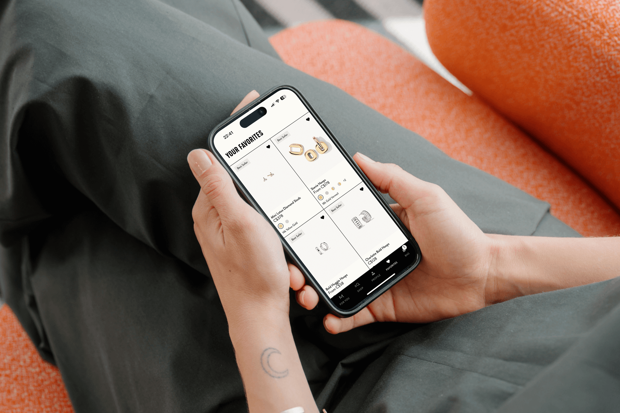 A person holding an iphone that's displaying the Mejuri App on the Favourites tab